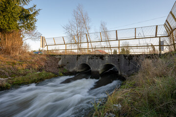 rushing water in the canal flowing through the double culvert - obrazy, fototapety, plakaty