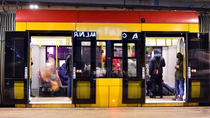 Lanterns and city lights are on In the background. People get on and get off city public tram .  © Grand Warszawski