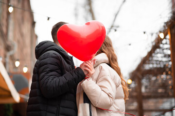 Couple holding a heart-shaped balloon and kissing on the street. Valentine's day concept, gifts,...
