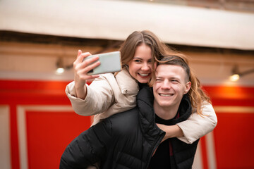 Close-up of a young man carrying a beautiful woman on his back. The couple takes a photo. Smiling girl sits on a guy looking at the camera. The guy rolls the girl on his back and smiles on the street