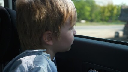 Little Boy Sits Waiting For Parents Return. Child Looking in Window. Kid Left Alone in Car Parked on Parking Lot. Summer Sunny Day. 2x Slow motion 60 fps 4K