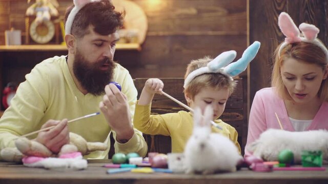 Happy family of mother, father and child son drawing easter eggs at home, painted eggs. Family celebrating easter with kids at home. Spring family holidays. Funny cute kids face.