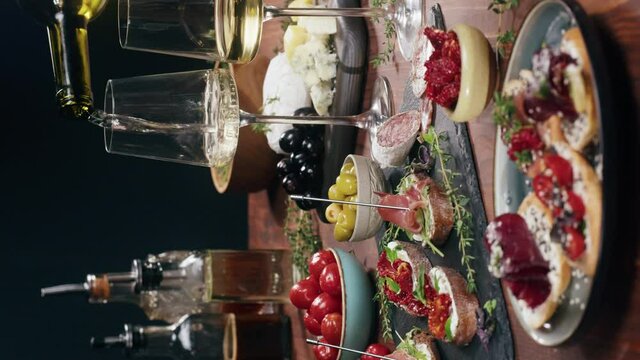 Vertical video, Italian restaurant with traditional food, Spanish cuisine, delicious tapas and white wine, bruschetta with cheese, olives dry tomatoes and tasty sandwich bar appetizer, buffet 