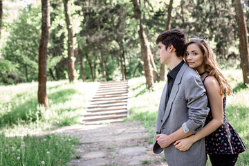 Naklejka premium Young couple walking in a spring park on Valentine's Day. The girl hid behind the guy's back while walking together in the park.