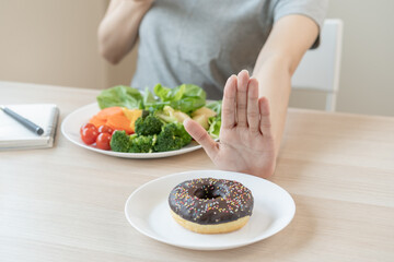Diet, Dieting asian young woman or girl use hand push out, deny sweet donut and choose green salad vegetables, eat food for good healthy, health when hungry. Close up female weight loss person.