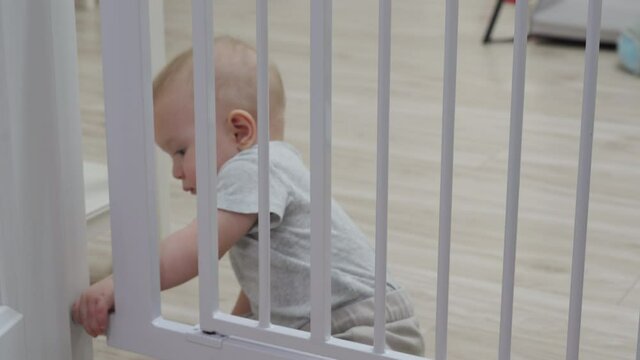 Childproofing house, doorway with safety baby gates to keep curious crawler away from dangerous areas of home, smart kid trying to open closed gate. Child safety proofing at home. 4k footage