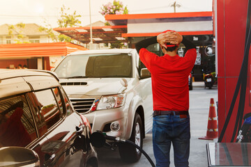 Rear view male worker dressed in a red shirt at a gas station is exhausted, with so many cars lined...