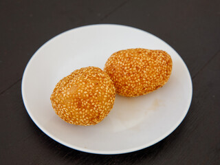 Khanom Kai Hong with sesame or Swan Eggs Dessert, native Thailand fried dessert balls like doughnuts on white plate on black wooden background