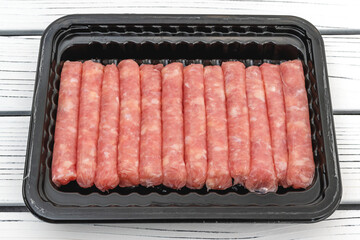 Raw chicken breakfast sausages in black plastic container close up on white wooden background