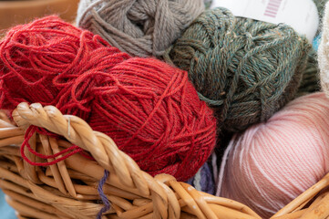 Basket of colorful yarn in a large wicker basket.  Red, gray, and pink skeins of cotton blend yarn, ready to be made into handmade items.