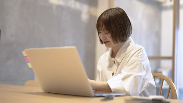 自宅の部屋でノートPCを操作する若い女性