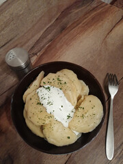 Homemade dumplings with sour cream in a black plate on a wooden table. Dumplings with hand-sculpted potato filling. Soft focus. Selective focus