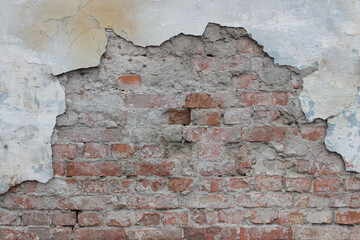 Old stone wall covered with cement. Half of cement on this wall is crumbled. There are bricks under the cement.	