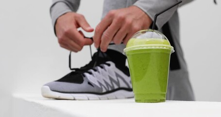 Green smoothie man tying running shoes laces ready to run in urban city. Healthy active lifestyle, closeup of trainers
