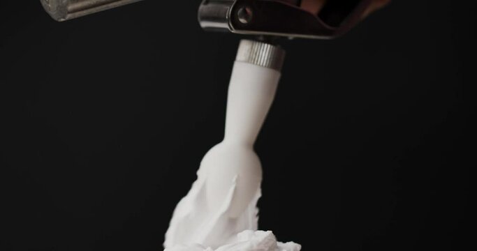 Squeeze the whipped cream into spiral waves. Smooth whipped cream on black background.