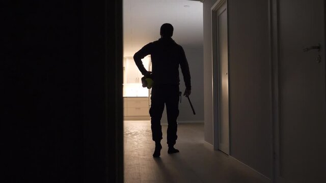 Contractor with tools, seen from behind, walks into empty room to look