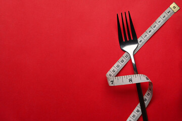 Fork with measure tape on red background with copy space for text. Healthy lifestyle concept.