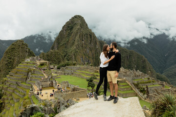 Happy young couple stands on the rock with Machu Picchu on the background, Cusco, Peru