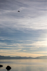 Tiny black plane silhouette in a big sky over the smooth surface of Lake Tahoe on a hazy day