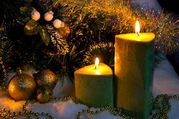 christmas decor decorated pine branches and burning wax candles on the snow with golden christmas tree decorations close-up