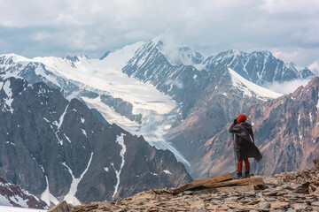 Hiker at very high altitude with view to long glacier tongue and high snow mountains under cloudy...