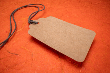 blank paper price tag with a twine against orange textured handmade paper, shopping concept