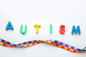 Word AUTISM and awareness ribbon on light background