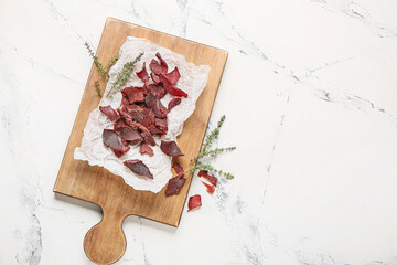 Board with spicy beef jerky on white background