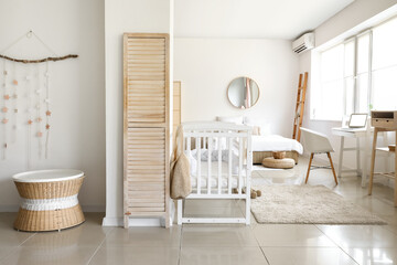 Interior of light bedroom with white crib and modern workplace