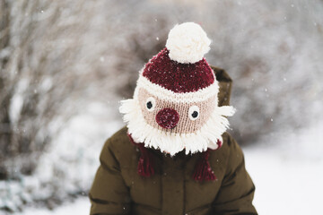 Child enjoying winter. Cute little boy in funny winter hat walks during a snowfall. Outdoors winter activities for kids. Winter Christmas and lifestyle concept.