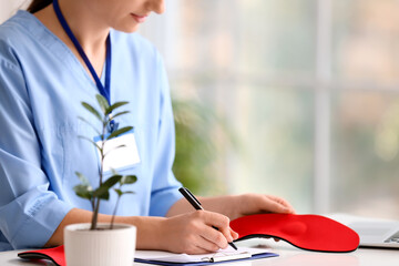 Female nurse making notes and holding red orthopedic insole at table