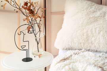 Vase with autumn branches and stylish decor on bedside table in bedroom