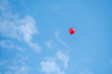 A red balloon flying under the blue sky and white clouds