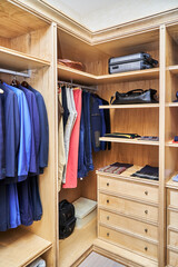 Stylish walk in closet with furniture of maple solid and veneer wood for clothes storage with crown molding in apartment