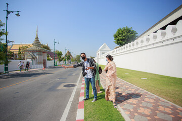 Obraz premium Three South Asian tourists with cameras happily hitchhiking the road behind Wat Pho during their long weekend happily. in Bangkok, Thailand