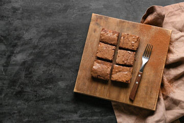 Wooden board with pieces of tasty chocolate brownie on black background