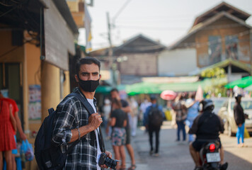 A South Asian tourist wearing a camera-printed shirt and backpack walks happily on a long weekend. in Bangkok, Thailand