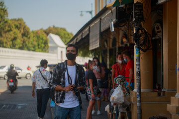 A South Asian tourist wearing a camera-printed shirt and backpack walks happily on a long weekend. in Bangkok, Thailand
