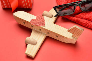 Wooden airplane with heart and sunglasses on red background, closeup. Valentine's Day celebration