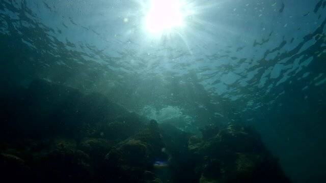 Under water film of tropical waters in Thailand - shallow water and rocks - bright sun shines through the water