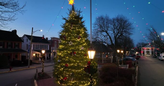 Rising aerial of large decorated Christmas tree to lights over small town in USA. Beautiful blue hour.