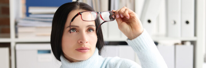 Woman takes off and looks at glasses while sitting at workplace