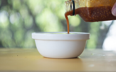 Spicy chili sauce drips out of a bottle into a bowl at home