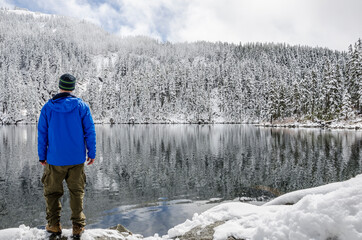 Winter sport activity. An athletic adventurous man standing on the shore of a winter lake surrounded by snow.