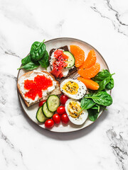 Breakfast, snack, tapas plate - sandwiches with red caviar, salmon, cream cheese, vegetables, spinach, boiled egg on a light background, top view