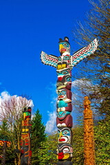 Obraz premium Three totem poles in Stanley Park, Vancouver surrounded by green trees and against a blue cloudy sky