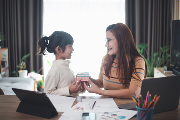 Happy Mother's day. Young woman mom getting congratulations from excited cute little daughter at home, child giving mother gift box while she working on laptop. Family holidays concept