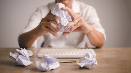 Closeup man crush the paper while , with many crumpled paper balls on the desk,