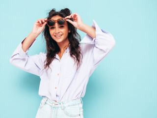 Young beautiful smiling female in trendy summer clothes. Sexy carefree woman posing near blue wall in studio. Positive brunette model having fun and going crazy. Cheerful and happy in sunglasses