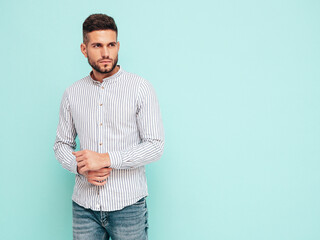 Portrait of handsome confident model. Sexy stylish man dressed in shirt and jeans. Fashion hipster male posing near blue wall in studio